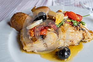 Closeup of a plate of good cod from the Atlantic sea with potatoes, onion, egg, red pepper, olives and coriander