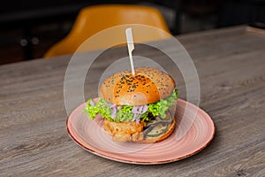 Closeup plate with juicy appetizing chicken burger isolated on wooden table background. Serving of big caloric sandwich