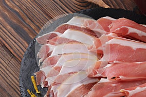 Closeup of a plate of prosciutto, an Italian dry-cured ham thinly sliced on a wooden brown background.