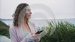 Closeup pleasant curly girl walking with smartphone at ocean background slow mo