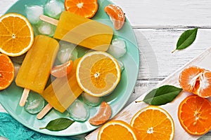 Closeup popsicle orange with slices of fresh orange, mandarin and green leaves on a white rustic plank table. Top view, flat lay