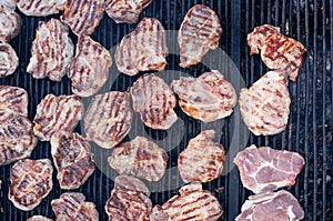 closeup of pork slices being grilled on black iron barbeque grate outdoors