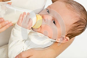 Closeup portrait of 3 months old baby boy holdin bottle with milk and eating
