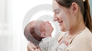 Closeup portrait of adorable little baby and smiling mother looking at each other against big window at house. Concept