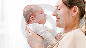 Closeup portrait of adorable little baby and smiling mother looking at each other against big window at house. Concept