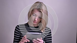 Closeup portrait of adult attractive blonde caucasian female using the tablet and looking at camera smiling with