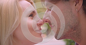 Closeup portrait of adult attractive caucasian couple looking at each other touching with their noses standing in park