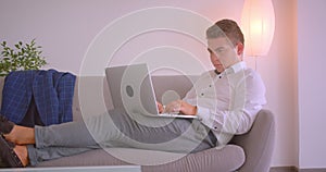 Closeup portrait of adult caucasian businessman using laptop sitting laidback on couch in office indoors