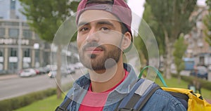 Closeup portrait of adult caucasian delivery man with backpack looking at camera smiling cheerfully in city outdoors