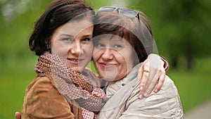 Closeup portrait of adult daughter and mother outdoors. Pretty brunette and her mom are looking at the camera in the