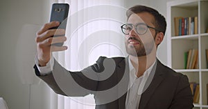Closeup portrait of adult handsome bearded caucasian businessman in glasses having a video call on the phone in the