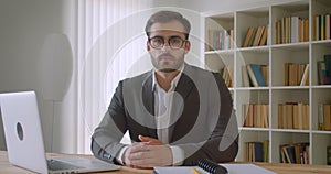 Closeup portrait of adult handsome caucasian businessman in glasses using the laptop looking at camera in the office