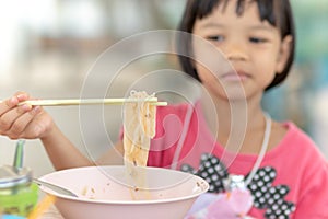 Closeup portrait Asian girl with short hair and cute face, aged 4 to 6 years old, using the right hand to hold the chopsticks