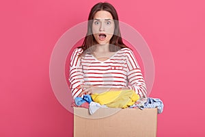 Closeup portrait of astonished female with widely opened mouth, lady with surprised facial expression holding box with clothes,