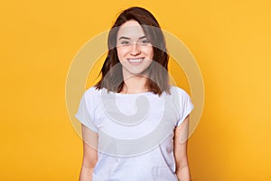 Closeup portrait of attractive woman stands smiling isolater over yellow background and looks directly at camera. Adorable lady