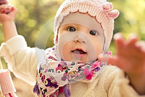 Closeup portrait of beautiful baby girl wearing stylish hat and cozy sweater. Outdoors spring, autumn photo.