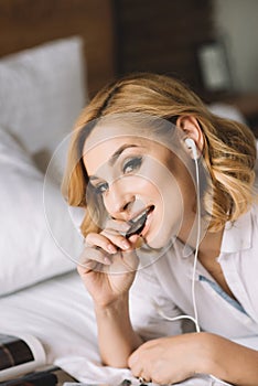 Closeup portrait of a beautiful blonde girl in headphones who eats chocolate and playfully looks into the camera
