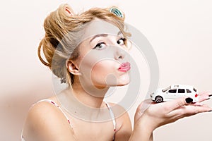 Closeup portrait of beautiful funny blond pinup girl with green eyes & curlers playing with car in the hands