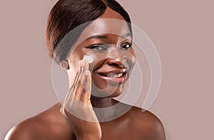 Closeup portrait of beautiful nude black woman applying moisturising cream on face