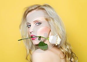 Closeup portrait of beautiful passionate woman in studio with bare shoulder and brigt makeup holding rose flower in photo