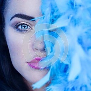 Closeup portrait of beautiful seductive brunette woman looking into the camera while playing with blue feather boa