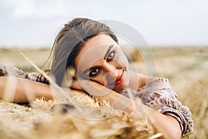 Closeup portrait of beautiful smiling woman with closed eyes. The brunette leaned on a bale of hay. A wheat field on the