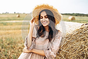 Closeup portrait of beautiful smiling woman with closed eyes. The brunette leaned on a bale of hay. A wheat field on the