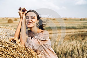 Closeup portrait of beautiful smiling woman with closed eyes. The brunette leaned on a bale of hay. A wheat field on the