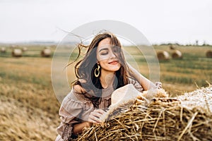 Closeup portrait of beautiful smiling woman with closed eyes. The brunette leaned on a bale of hay. A wheat field on the