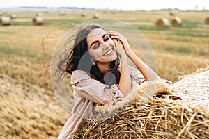 Closeup portrait of beautiful smiling woman with closed eyes. The brunette leaned on a bale of hay. A wheat field on the