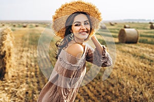 Closeup portrait of beautiful smiling woman with closed eyes. The brunette leaned on a bale of hay. A wheat field on the