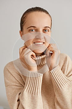 Closeup portrait of beautiful woman with ponytail wearing beige sweater looking at camera with happy optimistic facial expression