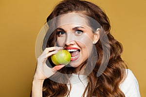 Closeup portrait of beautiful woman with white teeth and apple fruit on bright yellow background