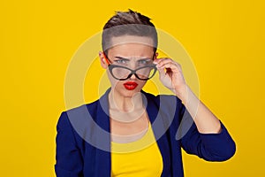 Closeup portrait beautiful young business woman lady looking at you camera over glasses gesture skeptically isolated yellow