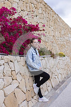 Closeup portrait of a beautiful young Caucasian teenager girl in a denim jacket posing outdoors in a park wall of natural stone