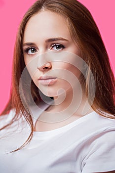 Closeup portrait of a beautiful young red haired girl on a pink background. A woman with clean skin and natural beauty