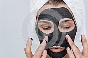 Closeup portrait of beautiful young woman applying clay black mask, doing beauty wellness treatment on her face skin. Horizontal