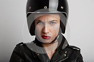 Closeup portrait of biker woman over white background, wearing stylish black sportive helmet and leather jacket.