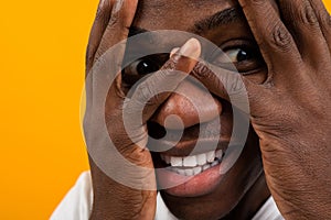 Closeup portrait of a blond handsome African black man covering his face with his hands in a white T-shirt on an orange