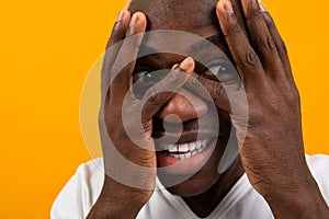 Closeup portrait of a blond handsome African black man covering his face with his hands in a white T-shirt on a yellow