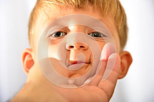 Closeup portrait of boy, little man`s hand holds baby by the face.