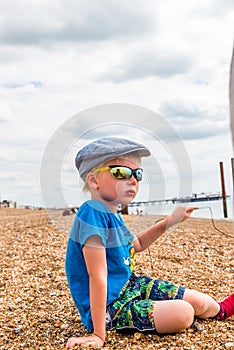 Closeup portrait of boy sitting on stone beach with sunglasses