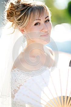 Closeup portrait of bride with fan outdoors in the sun.