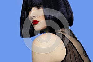 Closeup portrait of a brunette woman in black wig with make up, red lips, over blue background.