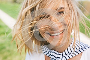 Closeup portrait of cheerful happy female with blonde blowing hair, smiling with toothy white healthy smile and looking at the