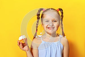 Closeup portrait of a cheerful little sweet tooth girl on a yellow background. The child smeared his nose with cream