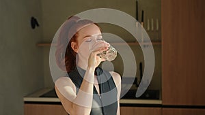 Closeup portrait of cheerful young sportswoman drinking clean mineral natural water in cup, satisfied after home