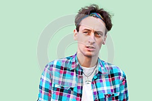 Closeup portrait of clever puzzlement young man in casual blue checkered shirt and headband standing, looking away and thinking to