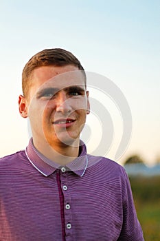 Closeup portrait of confused young brunette man in purple polo shirt standing outdoor on nature background at summer day
