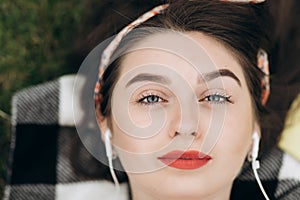 Close-up portrait of content young beautiful woman wearing headphones, listening to music with her eyes open and lying